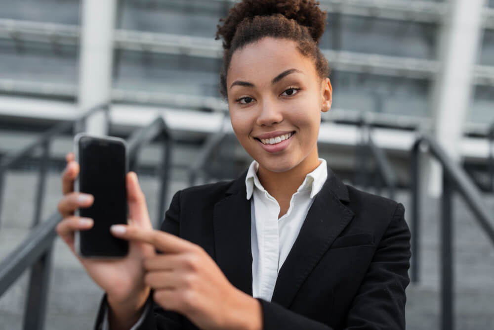 Mulher sorrindo segurando um celular com a mão esquerda