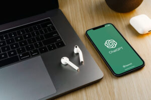 Notebook em uma mesa com fones sem fio e um celular com a logo do chatgpt