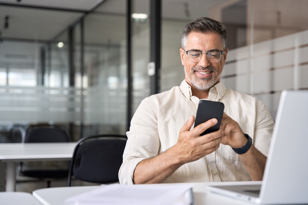 Homem sorrindo, mexendo no celular com ele à mão