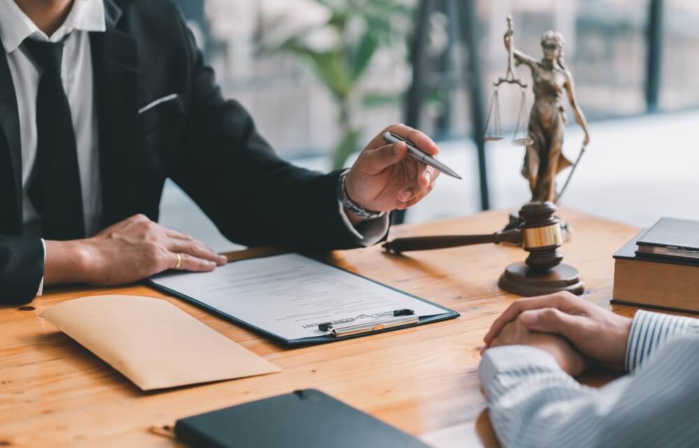 advogado com malhete na mesa e uma balança do direito conversando com cliente