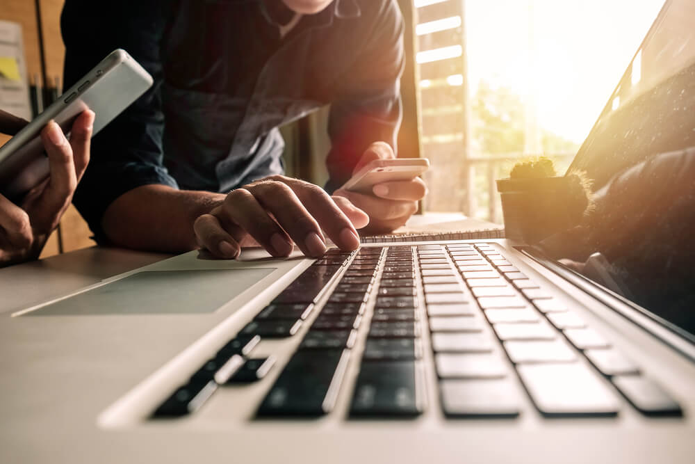 Dois homens com celular na mão, um deles com a mão em um notebook