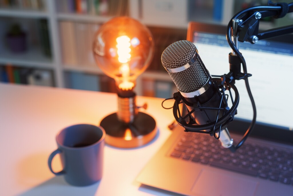 Mesa com notebook, caneca, lâmpada, notebook e microfone para podcast